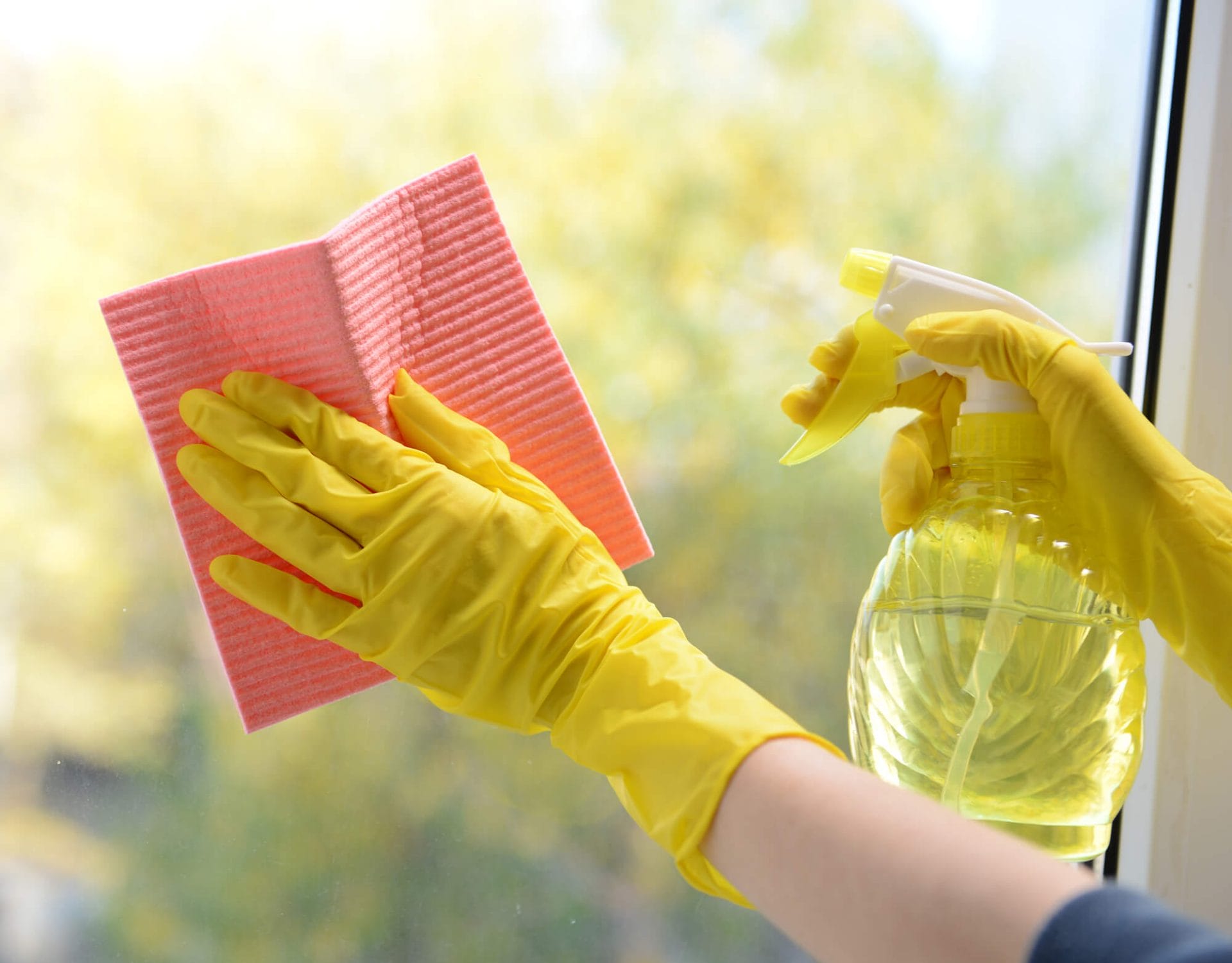 A person spraying the window glass and wiping it with a pink rag and yellow gloves